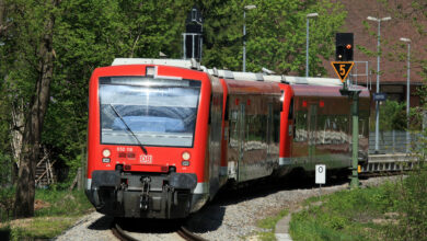 Ein roter Diesel-Personenzug fährt auf einem Gleis entgegen.