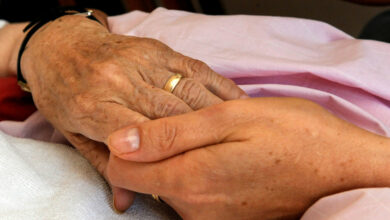 Eine Pflegerin hält die Hand einer todkranken Patientin (Bild: © dpa)