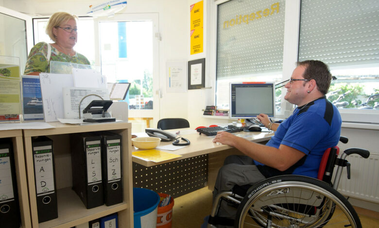 Ein Mann im Rollstuhl arbeitet an der Rezeption eines Campingplatzes. (Foto: © dpa)