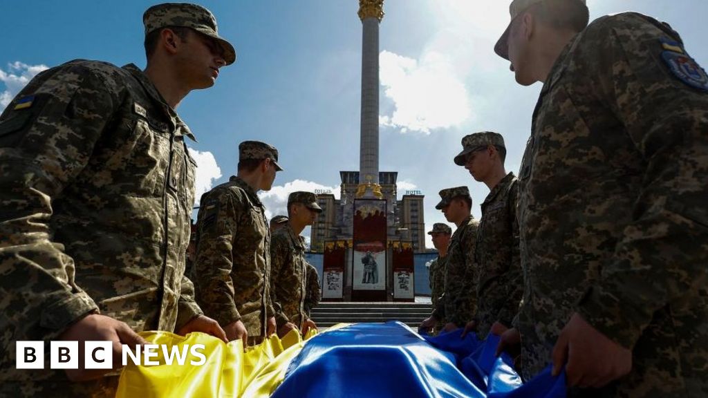 Ukrainian troops hold a Ukrainian flag over a coffin of a serviceman