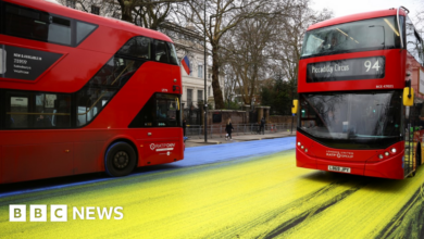 Two buses drive through the yellow and blue paint left by protestors outside the Russian embassy