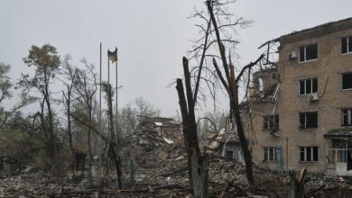 Verkohlte Bäume, eine einzelne ukrainische Flagge und die Überreste eines zerstörten Gebäudes in Avdiivka, Ukraine