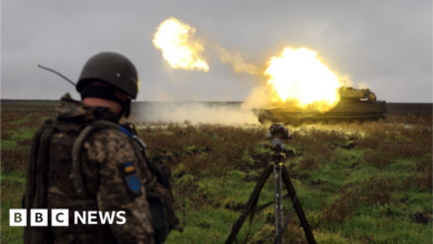 A Ukrainian soldier stands beside a self-propelled gun as it is fired.